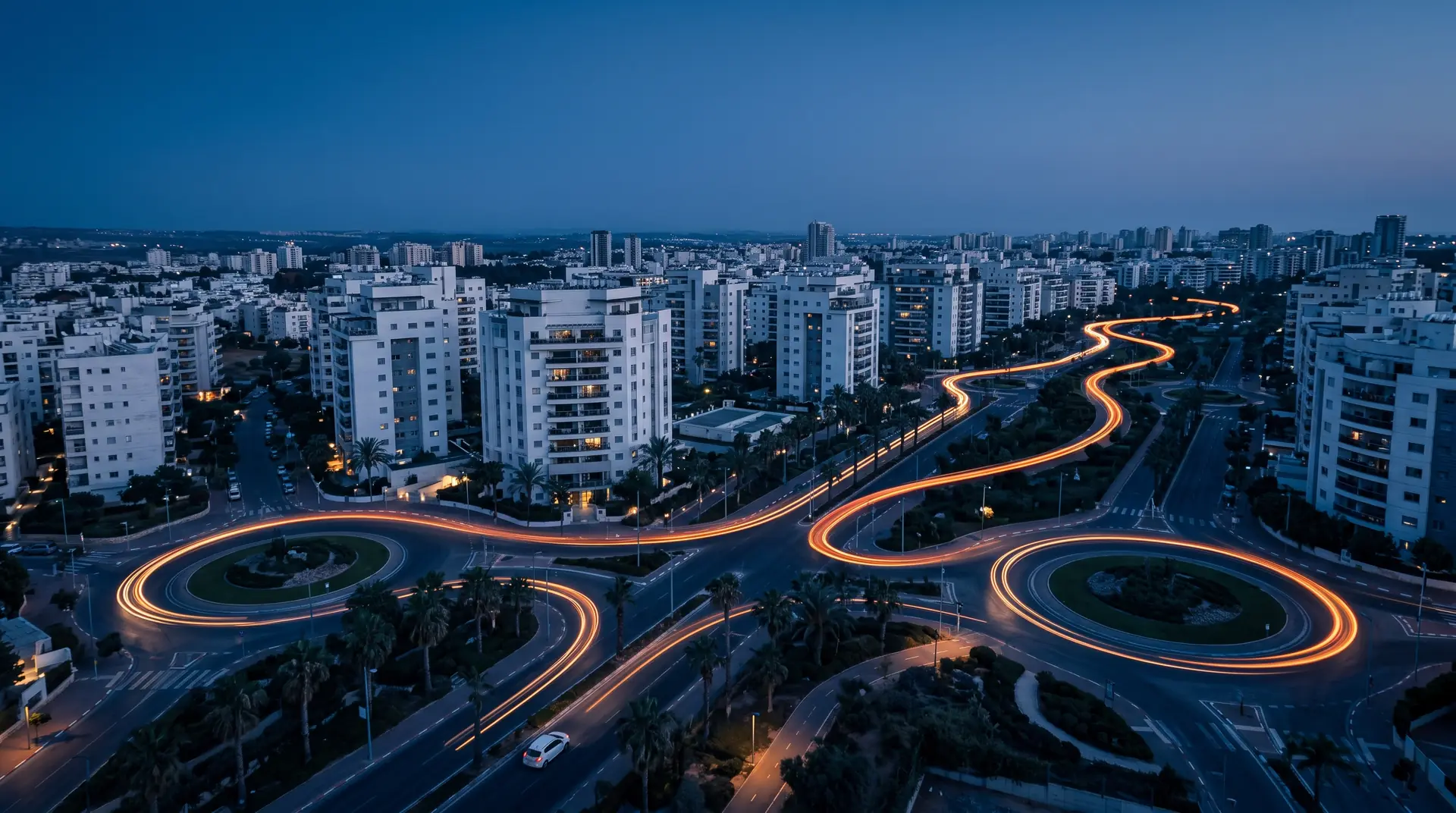 מבט מלמעלה על שדרות וכיכרות בעיר בשעת דמדומים, ופס אור של רכב שמתפתל ביניהן